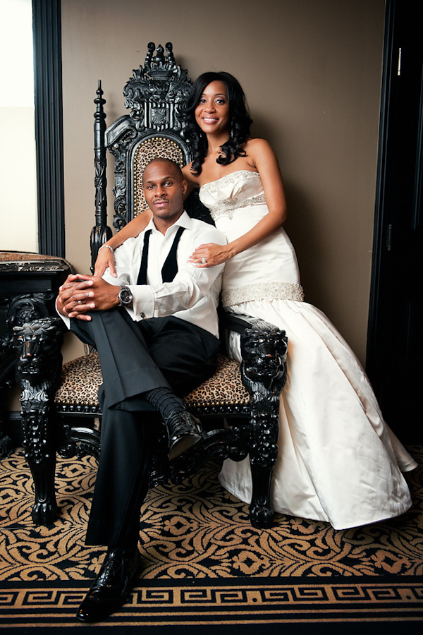 the happy couple - the groom wearing black and white tuxedo without the jacket and bow tie hanging around his neck sitting in an elaborate antique chair as bride stands next to him wearing a champagne mermaid style dress - photo by Houston based wedding photographer Adam Nyholt